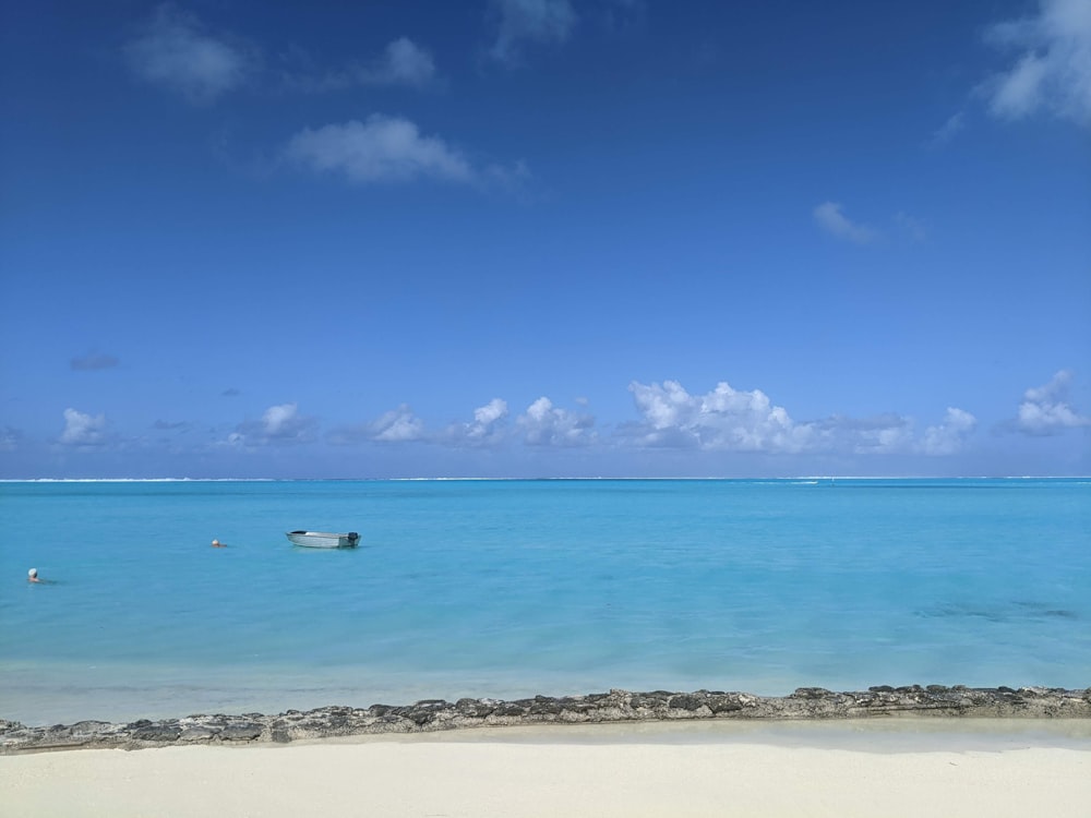 a boat floating on top of a blue ocean next to a sandy beach