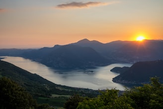 A serene landscape depicting a calm lake surrounded by mountains during sunset.