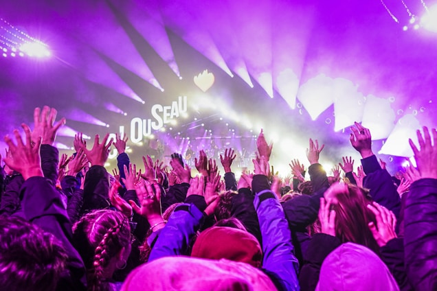 A vibrant crowd raising hands in worship under colorful stage lights.