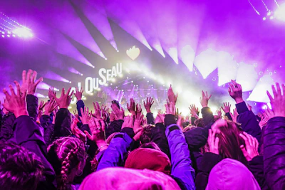 Dynamic crowd with raised hands illuminated by neon yellow and aqua blue stage lights during a youth revival event.