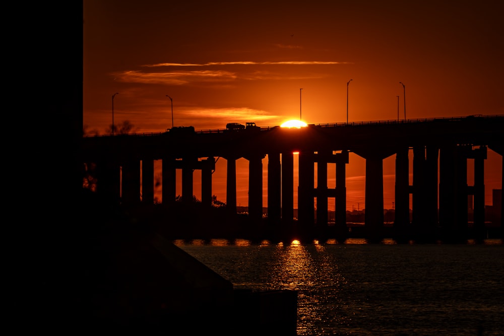 the sun is setting over a bridge over a body of water