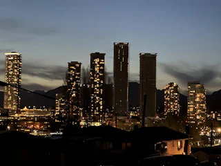 Horizontal shot of a city skyline at dusk with glowing windows and a dark sky.