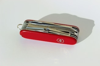 A red multi-functional pocket knife with various foldable tools with a white cross emblem on its side.