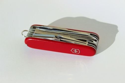 A red multi-functional pocket knife with various foldable tools with a white cross emblem on its side.
