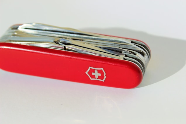 A Swiss Army knife featuring multiple tools folded within a bright red handle. The emblem of a white cross within a shield is prominently displayed on the side.