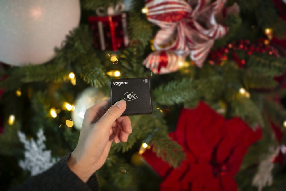 a person holding up a black box in front of a christmas tree