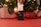 A hand is holding a white credit card above a contactless card reader. The background features a decorated Christmas tree with lights and wrapped gifts in red and white patterns.