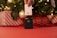 A hand is holding a white credit card above a contactless card reader. The background features a decorated Christmas tree with lights and wrapped gifts in red and white patterns.
