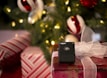 A black wireless payment terminal by Vagaro is placed on a wrapped gift box with a white mesh bow. The background features a decorated Christmas tree with illuminated lights and ornaments in red, white, and green colors.