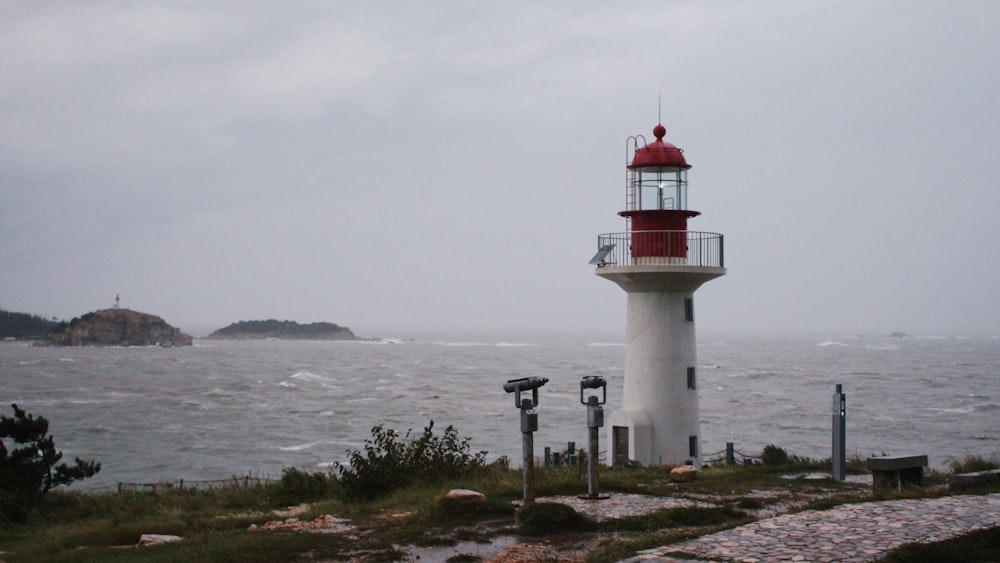 a red and white light house sitting on top of a hill next to the ocean