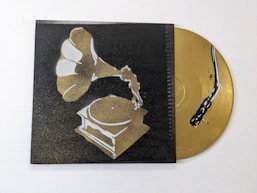 A stylized image of a gramophone painted in shades of gold and white against a dark background. Beside it, a golden vinyl record with a stylized black snake design is partially visible.