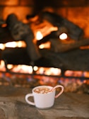 A fireside scene with a person wrapped in a thick cardigan, holding a mug of hot cocoa.