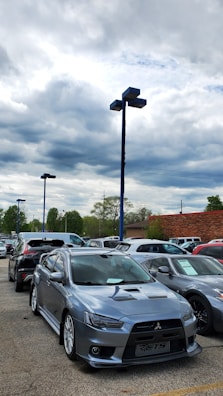 A row of well-used cars parked on a gravel lot under a cloudy sky.