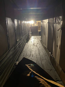 A dimly lit industrial corridor with flickering fluorescent lights, dripping pipes, and a faint silhouette in the fog.