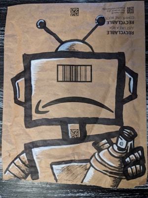 A paper bag features a stylized drawing of a robot holding a spray can. The robot has a large rectangular head with a barcode on its face and two antennae on top. The bag also includes QR codes and recyclable information printed at the top.