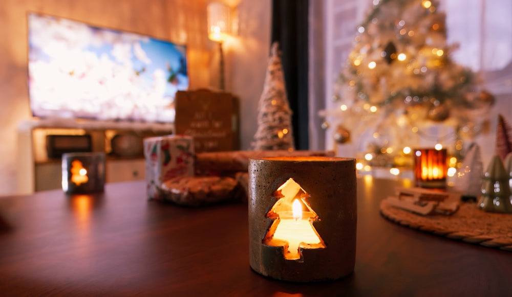 a lit candle on a table in front of a christmas tree