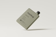 A rectangular plastic bottle with a minimalist design, featuring a black cap. The bottle is khaki-colored and is labeled with the word 'mockup' along with additional text indicating it's a plastic bottle. The background is a light cream color, and the bottle appears to be floating.