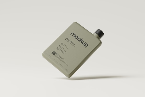 A rectangular plastic bottle with a minimalist design, featuring a black cap. The bottle is khaki-colored and is labeled with the word 'mockup' along with additional text indicating it's a plastic bottle. The background is a light cream color, and the bottle appears to be floating.