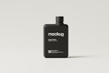 A black plastic bottle with a modern, minimalist design sits on a light, neutral background. The bottle is labeled 'mockup' in a clean, white font, and includes additional text indicating it is a plastic bottle mockup template available at mocksupply.net. A QR code is visible at the bottom of the label.