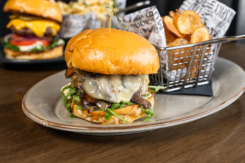 A gourmet burger topped with caramelized onions, melted cheese, and fresh greens on a rustic wooden board.