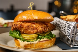 a chicken sandwich on a plate next to a basket of fries