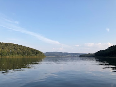 A serene lake reflecting the surrounding hills under a clear blue sky near the homestay.