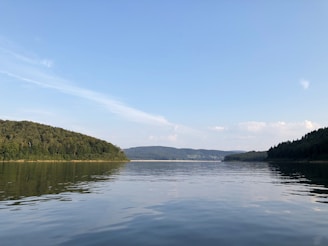 A serene lake reflecting the surrounding hills under a clear blue sky near the homestay.