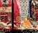 A festive display with toy kitchen sets, stuffed animals, and a variety of children's toys surrounded by decorative lights and a red backdrop. The scene is adorned with a snow-covered wreath and miniature Christmas trees, creating a cozy holiday atmosphere.