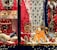 A festive display with toy kitchen sets, stuffed animals, and a variety of children's toys surrounded by decorative lights and a red backdrop. The scene is adorned with a snow-covered wreath and miniature Christmas trees, creating a cozy holiday atmosphere.