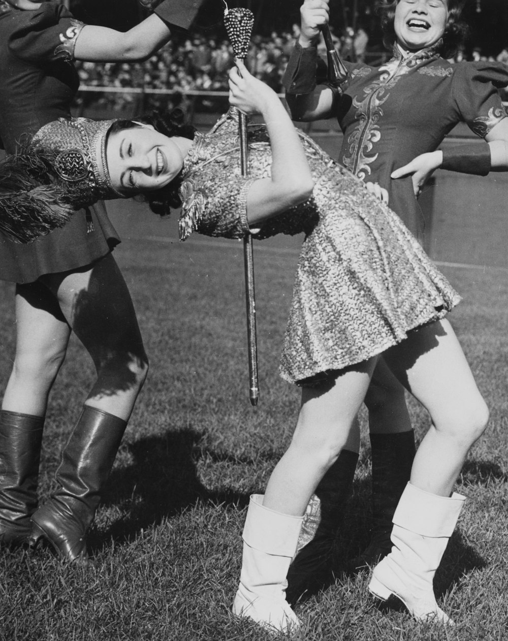 lead majorette, Rita Phillips, doing a back bend while holding a baton; two other majorettes marching on field behind Phillips