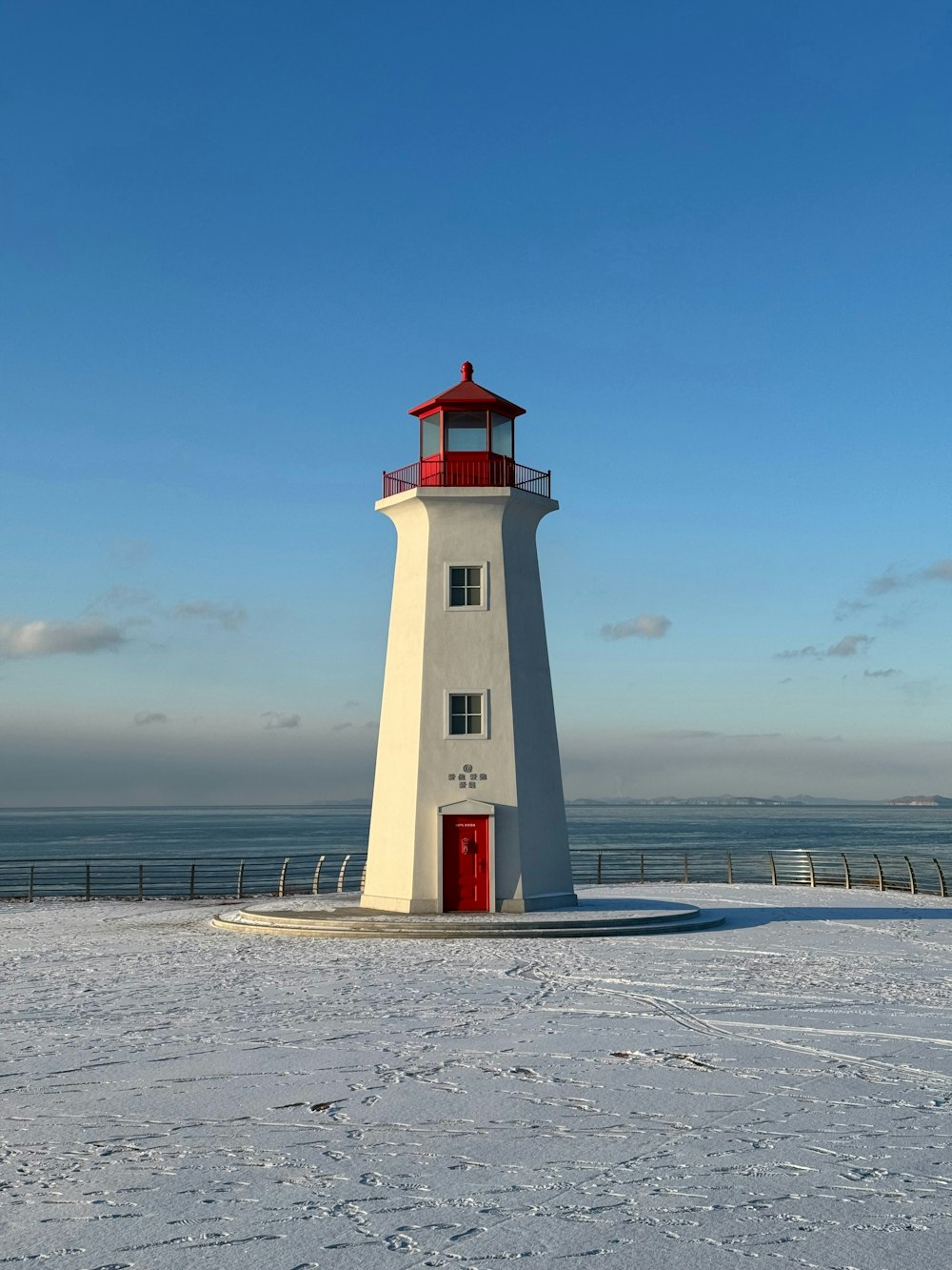 a white lighthouse with a red door in the snow