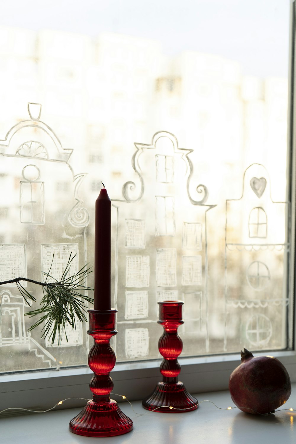 a window sill with two red candles and an apple