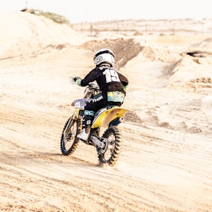 A rider gearing up with motocross accessories against a backdrop of dirt tracks.