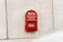 A bright red Emirates Post letter mailbox is mounted on a textured, off-white concrete wall. The surface of the wall is slightly stained near the bottom of the mailbox. Arabic and English text are clearly visible on the mailbox, along with the Emirates Post logo.