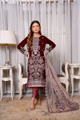 A graceful Algerian woman in a richly embroidered traditional dress, standing against a warm, softly lit backdrop.