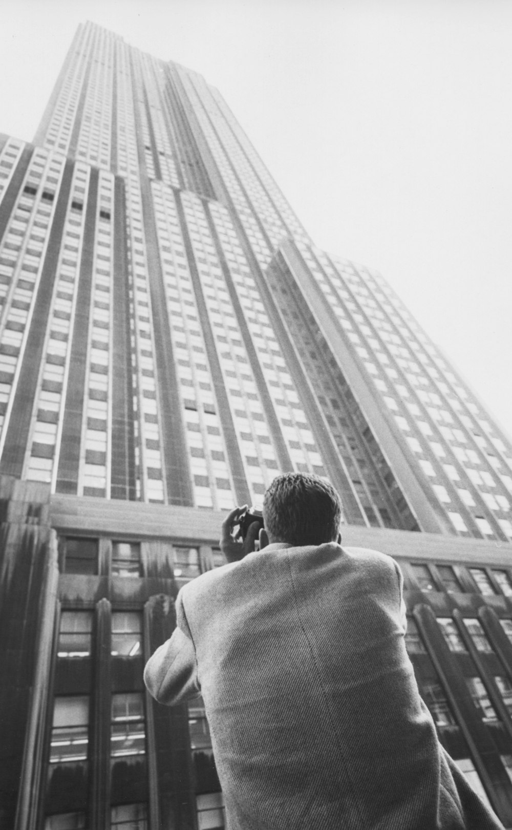 The big one Summary Photograph shows a man from behind and below, taking a photo of the Empire State building