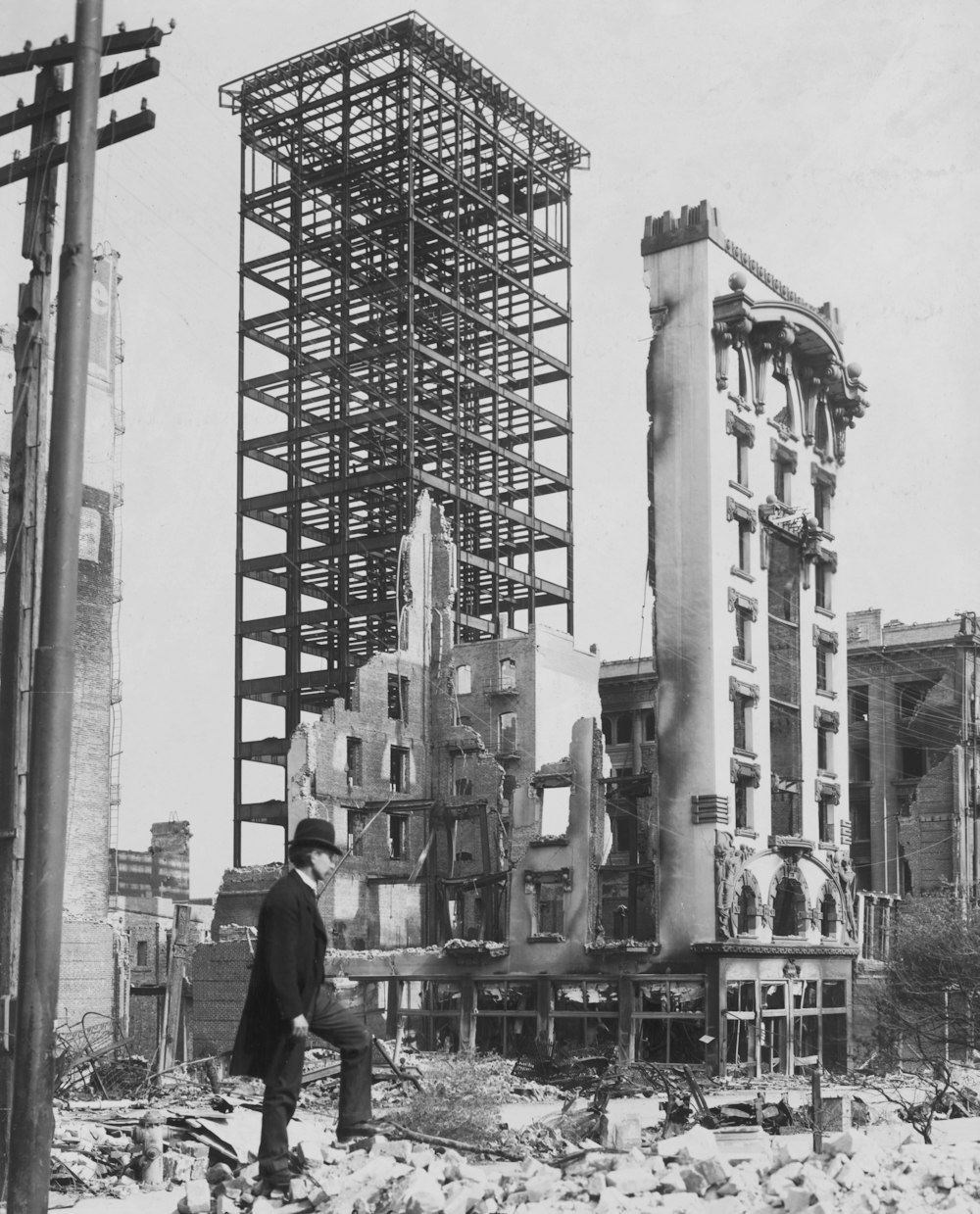 Unfinished steel structure intact after quake, San Francisco Summary Photo shows the San Francisco earthquake and fire disaster with a man standing among rubble in foreground and an unfinished but intact steel structure in background and remnants of burned out brick and stone buildings nearby 