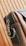 A close-up of a stylish leather bag with a metal zipper and a sturdy metal ring on its side. The bag's material appears smooth and high-quality, with careful stitching visible along the edges. The background features a wooden pattern with vertical lines.