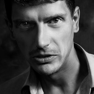 A close-up black and white portrait of Juan Baraza deeply immersed in character, with intense shadows highlighting his expression.