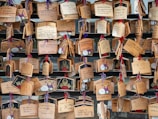 A collection of wooden plaques with various handwritten messages, some decorated with illustrations. The plaques are hung with colorful strings on a wooden structure, creating an arrangement of wishes or prayers.
