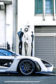 A shiny white sports car with gleaming gold accents parked on a modern city street.