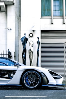 A shiny white sports car with gleaming gold accents parked on a modern city street.