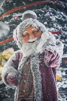 A festive figure resembling Santa Claus is adorned with icy, snow-like textures. This figure features a joyful expression, a red and white outfit, and a full, snowy beard, set against a background of a decorated, snow-covered Christmas tree with colorful lights.