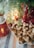 A festive scene with gingerbread cookies shaped like trees on a white plate. Evergreen branches hang above with red ornaments and warm string lights creating a cozy atmosphere. A red ceramic candle holder shaped like a house adds to the holiday decor.