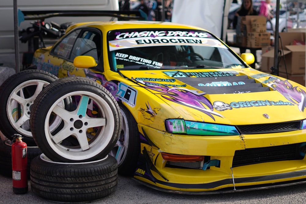 a yellow car is parked next to a pile of tires