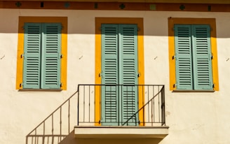 a white building with blue and yellow shutters and a balcony