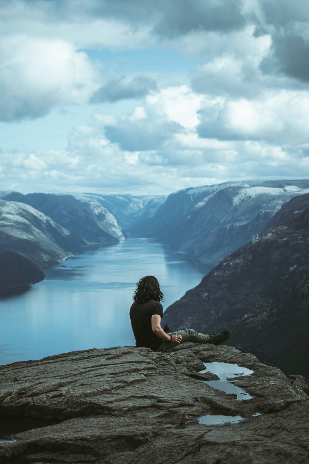 a woman sitting on top of a rock next to a body of water