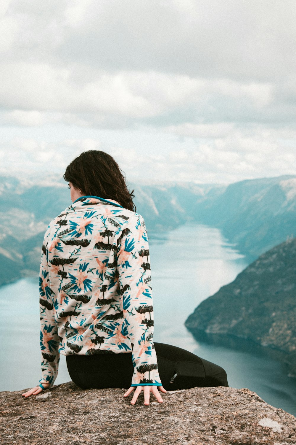 a woman sitting on top of a cliff overlooking a body of water