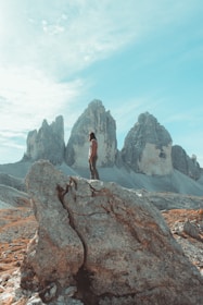 Adventurous traveler standing atop rugged mountain peak overlooking vast landscapes.