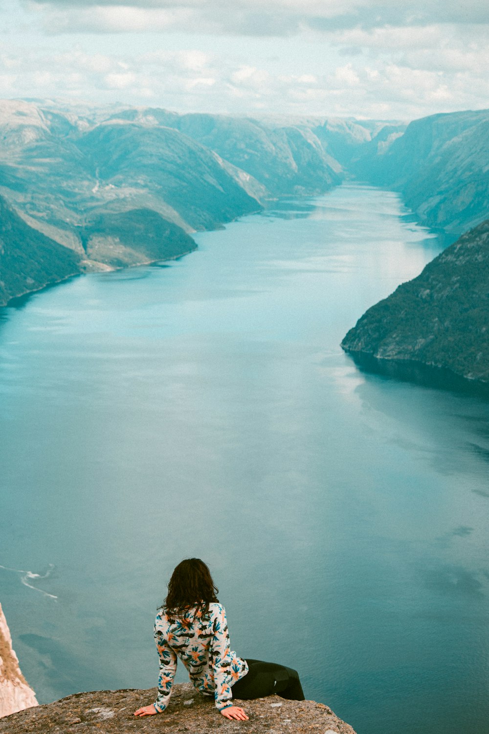 a woman sitting on top of a rock next to a body of water